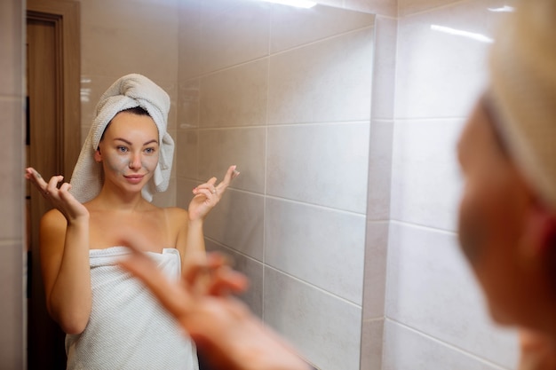 Spa e cosmetologia, cuidados com a pele facial em casa garota no banheiro aplica uma máscara facial de creme
