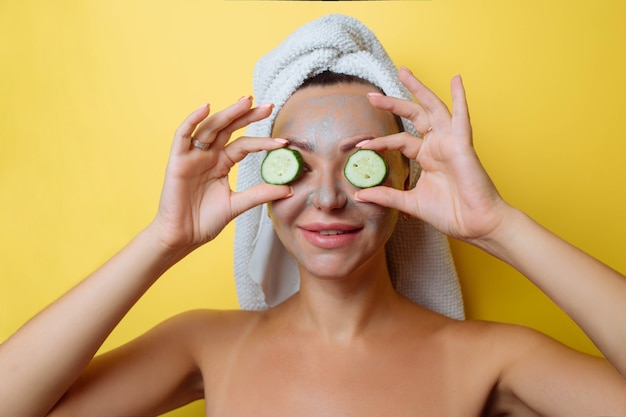 Spa e cosmetologia. Cuidados com a pele facial. Uma menina depois do banho com uma toalha na cabeça e pepinos em seu close-up de olhos.