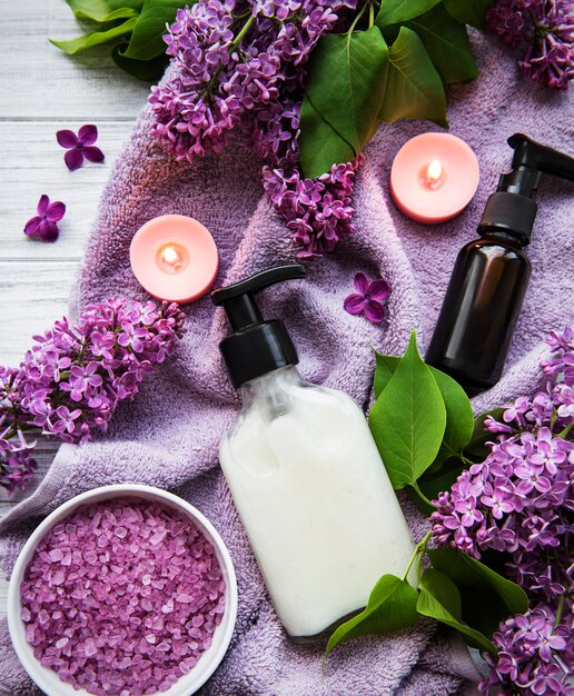 Spa-Einstellung mit lila Blumen. Meersalz in Schüssel, Flaschen mit Aromaöl und Kerzen auf Holzoberfläche.