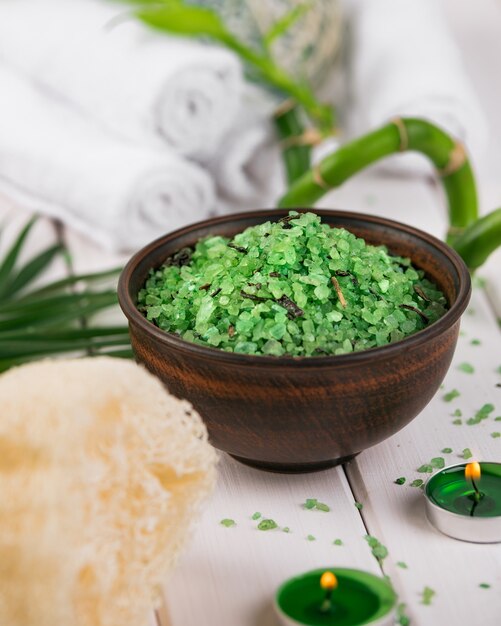 Spa. Grünes Kräuter-Spirulina-Salz in Keramikschale, Spa-Handtüchern, Kerzen und Bambus.