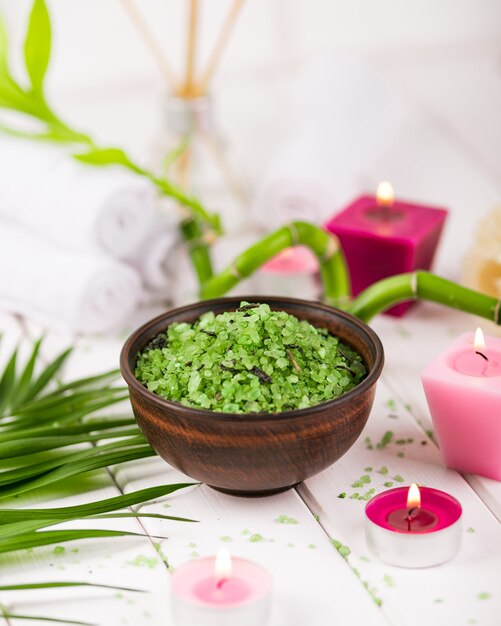 Spa. Grünes Spirulina-Kräutersalz in Keramikschale, Badetücher, rosa Duftkerze und Bambus.