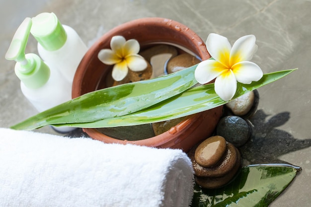 Spa o flores de bienestar con cuenco de hojas tropicales de toalla de agua y tubos de crema sobre fondo oscuro Cuidado corporal y concepto de spa