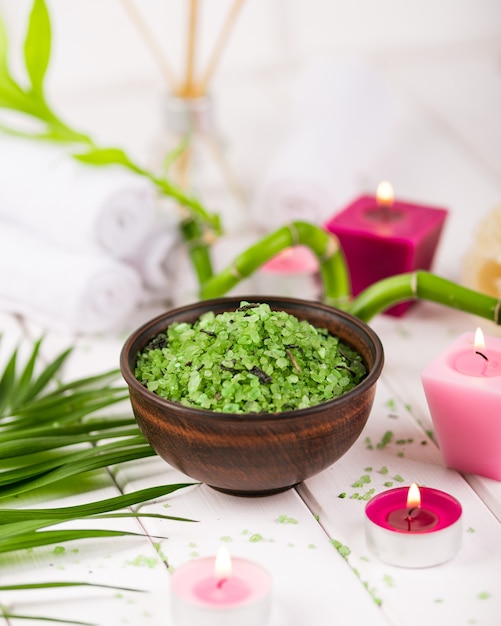 Spa. Sal de espirulina de hierbas verdes en cuenco de cerámica, toallas de spa, vela perfumada rosa y bambú.