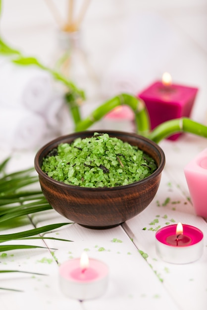 Spa. sal verde de espirulina de ervas em uma tigela de cerâmica, toalhas de spa, vela rosa perfumada e bambu.