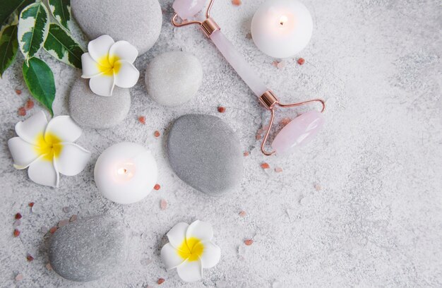 Spa-Set, ätherisches Öl, Massagesalz, Kerze und Frangipani-Blüten auf grauem Betonhintergrund