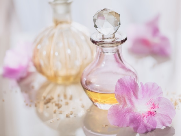 Spa-Stillleben mit Parfüm- und Aromaölflaschen, umgeben von Blumen, auf heller Oberfläche