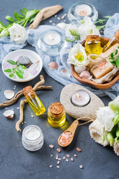 Spa-Stillleben-Wellness-Einstellungskonzept Sortiment an ätherischen Ölen, Meersalz, Naturseifenkerzen, weißen Frühlingsblumen und Handtuch auf einem schwarzen Tisch