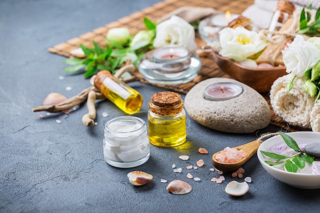 Spa-Stillleben-Wellness-Einstellungskonzept Sortiment an ätherischen Ölen, Meersalz, Naturseifenkerzen, weißen Frühlingsblumen und Handtuch auf einem schwarzen Tisch