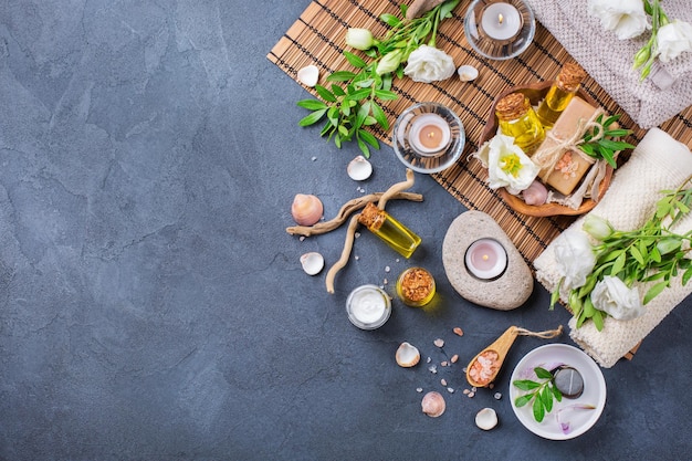 Spa-Stillleben-Wellness-Setting-Konzept Auswahl an ätherischen Ölen, Creme, Meersalz, natürliche Seife, Kerzen, weiße Frühlingsblumen und Handtuch auf einem schwarzen Tisch, Draufsicht auf den Hintergrund des Kopierraums