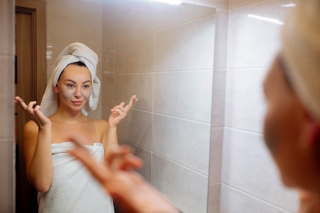 Spa- und Kosmetik-Gesichtshautpflege zu Hause Mädchen im Badezimmer trägt eine Creme-Gesichtsmaske auf