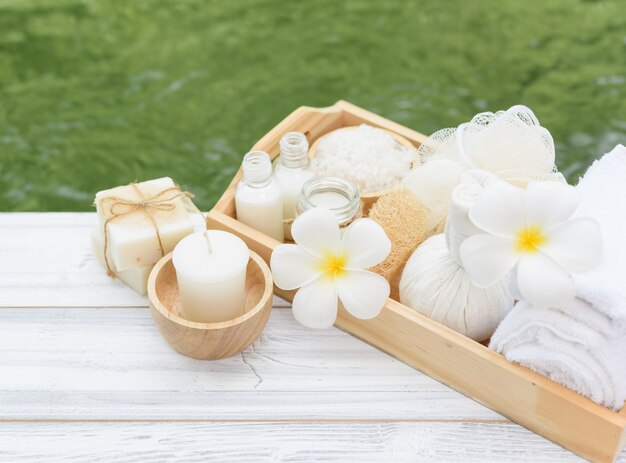 Spa-Wellness-Konzept, weiße Kerze, Milchseife, Salz, Handtuch, Blumen und Kräutermassageball auf weißem Holztisch