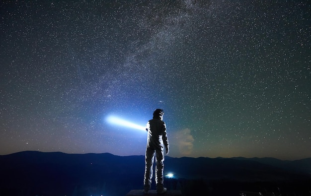 Spaceman dirige un rayo de luz hacia el cielo con la ayuda de una linterna en la noche en las montañas
