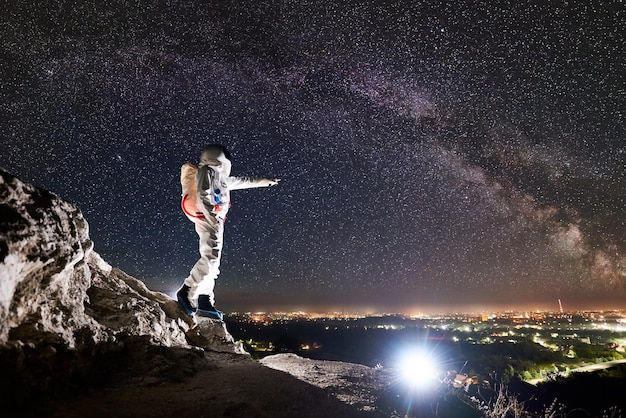 Spaceman em pé na montanha rochosa sob lindo céu estrelado