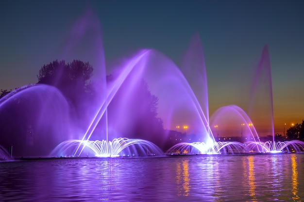 Spätabends im Sommer in der Stadt. Brunnen am Fluss mit Lichtern