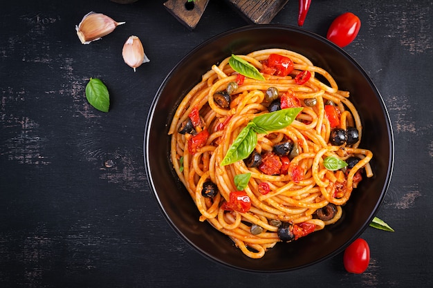 Spaghetti alla puttanesca - italienisches Nudelgericht mit Tomaten, schwarzen Oliven, Kapern, Sardellen und Basilikum. Ansicht von oben, flach