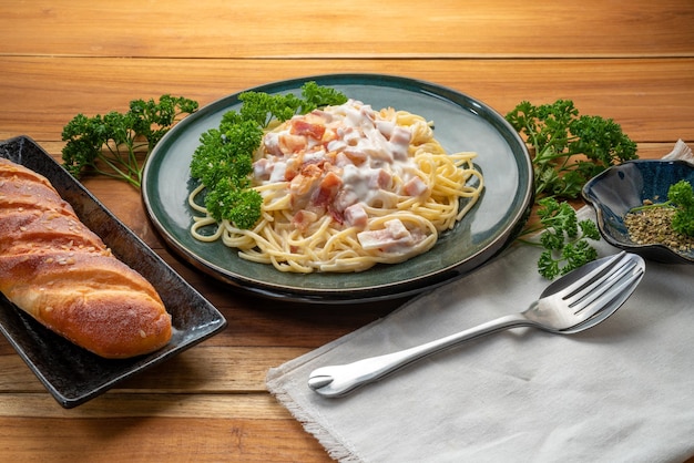 Spaghetti carbonara con jamón y tocino en plato verde sobre mesa de madera