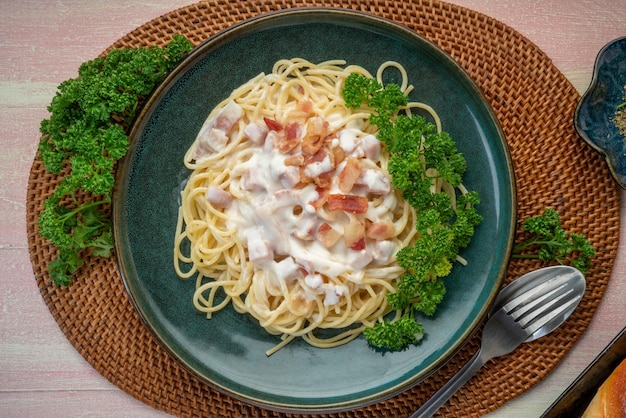 Spaghetti carbonara con jamón y tocino en plato verde sobre mesa de madera