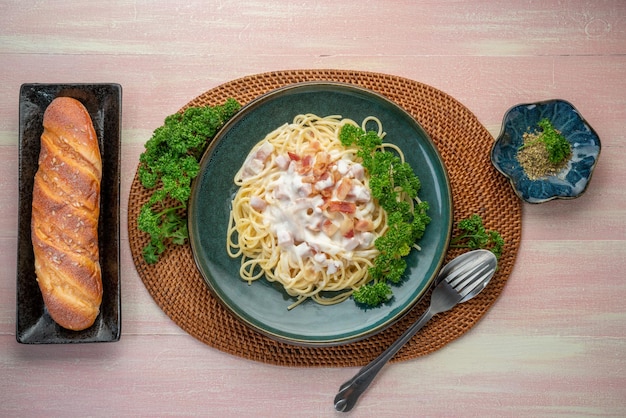 Spaghetti carbonara con jamón y tocino en plato verde sobre mesa de madera