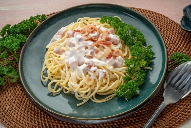 Spaghetti Carbonara mit Schinken und Speck auf grünem Teller auf Holztisch