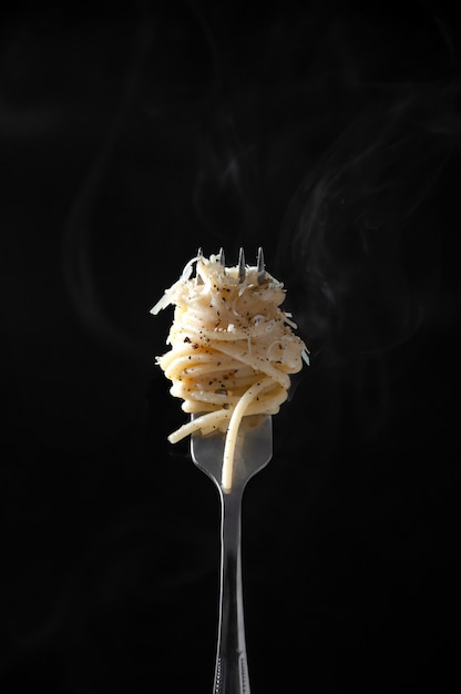 Foto spaghetti en horquilla con vapor sobre fondo oscuro