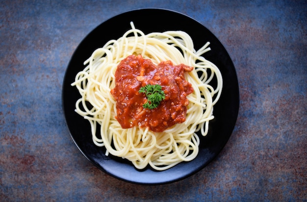 Spaghetti italienische Pasta serviert auf schwarzem Teller mit Tomatensauce und Petersilie im Restaurant italienisches Essen und Menükonzept / Spaghetti Bolognese