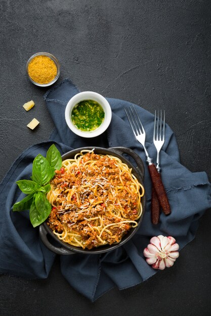 Foto spaghetti mit bolognese-sauce, oliven und gewürzen auf schwarzer oberfläche