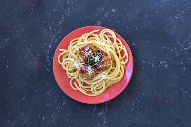 Spaghetti mit Fleischbällchen, Tomatensauce und Parmesan in einem roten Teller