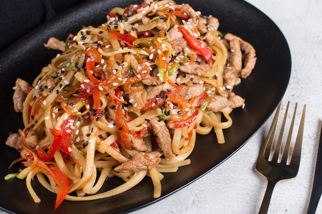 Spaghetti mit Gemüsesoße und Fleisch auf einem schwarzen Teller das Konzept des Restaurants, das Gerichte Wok serviert