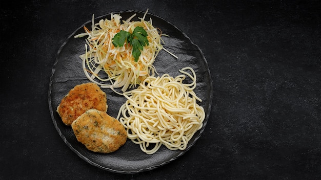 Spaghetti mit Kotelett und Salat auf einem schwarzen Teller