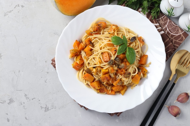 Spaghetti mit Kürbis und Kürbiskernen in einem weißen Teller auf einem Grau.