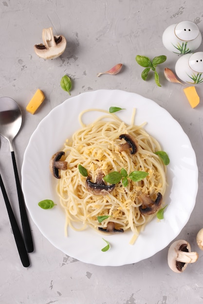 Spaghetti mit Pilzen und Basilikum auf weißem Teller auf grauem Hintergrund, Nahaufnahme