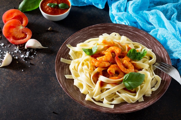 Spaghetti mit Tomatensauce und Garnelen in einem Teller auf dunklem Betonstein oder Schieferhintergrund