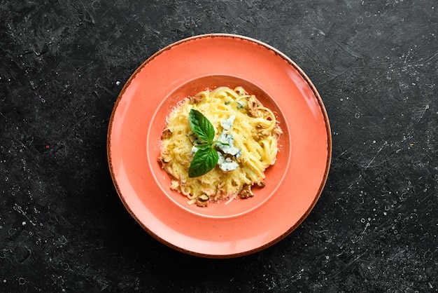 Spaghetti-Nudeln mit Käse und Basilikum in einem Teller auf schwarzem Steinhintergrund