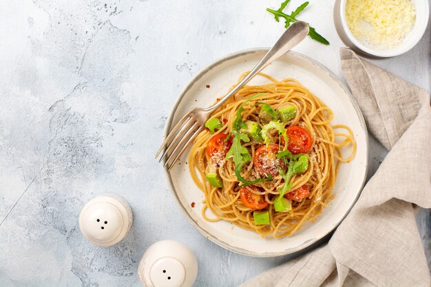 Spaghetti-Nudeln mit Pesto, Avocado und Tomaten im rustikalen weißen Teller. Rohes veganes Lebensmittelkonzept. Ansicht von oben.