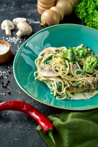 Spaghetti-Nudeln mit Pilzen, Brokkoli und weißer Soße auf einem Teller auf dunklem Hintergrund. Vegetarische Nudeln