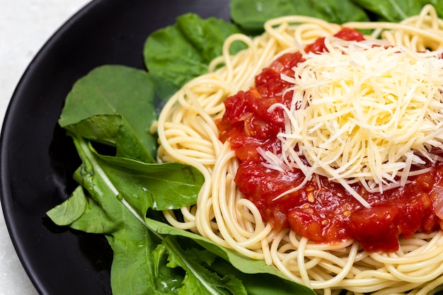 Spaghetti-Nudeln mit roter Sauce, Rucola und Parmesan auf schwarzem Teller mit weißem Marmorhintergrund