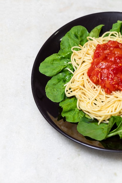 Spaghetti-Nudeln mit roter Sauce und Rucola auf schwarzem Teller mit weißem Marmorhintergrund