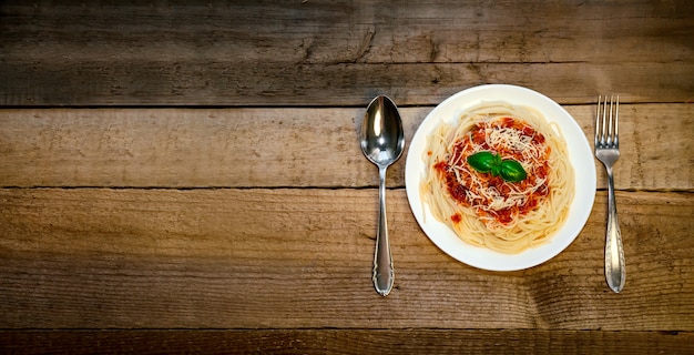 Spaghetti-Nudeln mit Tomatensauce, Käse und Basilikum auf Holztisch. Traditionelles italienisches Essen. Banner. Draufsicht Flat Lay.