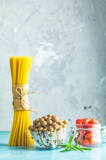 Spaghetti Shimeji-Pilz, Olivenöl, rosa Salz, leere Keramikschüssel, Holzlöffel für Salat auf blauem Betonhintergrund, gesundes Ernährungskonzept, Kopierraum für Ihren Text