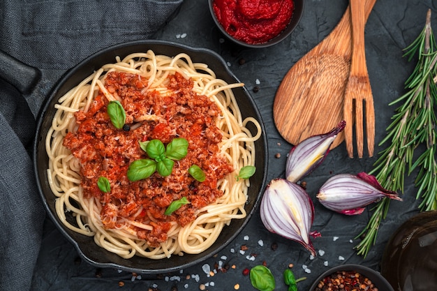 Spaghetti und Tomatensauce mit Hackfleisch und frischem Basilikum auf schwarzem Grund. Draufsicht