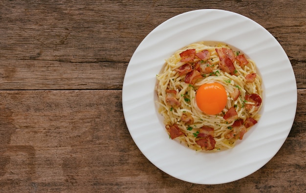 Spaghettis carbonara mit Speck, Käse, Eigelb und gehackter Petersilie auf hölzerner Tabelle in der Draufsicht