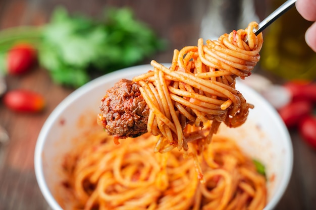 Spaghettis und Fleischklöschen mit Tomatensauce in der weißen Schüssel auf hölzernem rustikalem Brett
