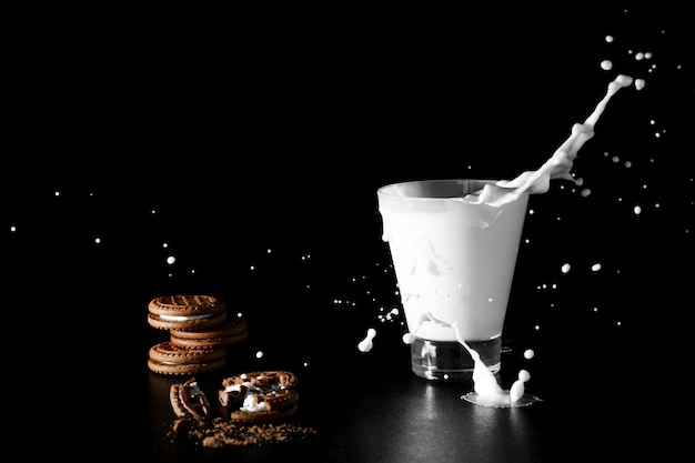 Spalsh em copo de leite e chocolate cookies em fundo preto