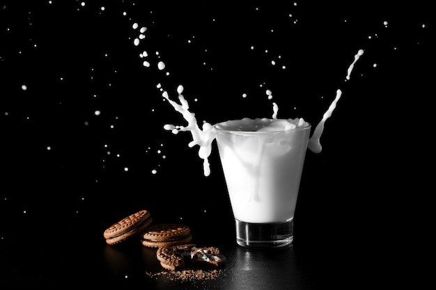 Spalsh en vaso de leche y galletas de chocolate sobre fondo negro