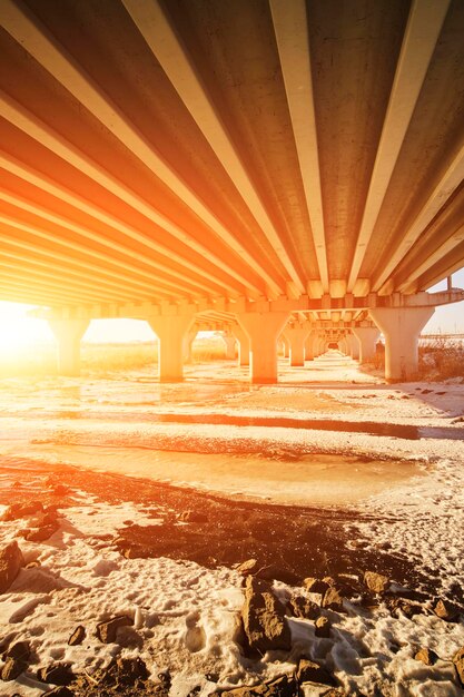 Spalten Kraftverkehr Brücke Hintergrund Sonnenuntergang und ein zugefrorener Fluss unter der Brücke