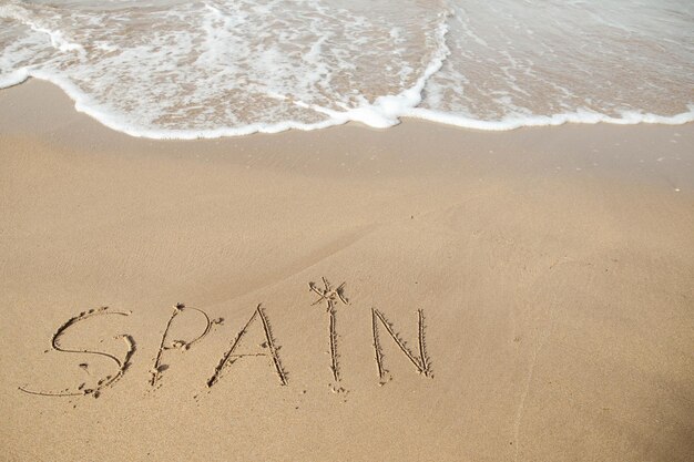 Spanien-Schriftzug am Sandstrand und Meerwasser
