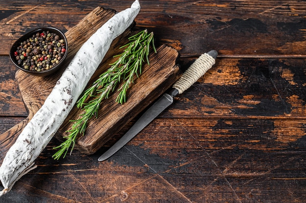 Spanische Fuet-Salamiwurst auf einem Holzbrett. Dunkler hölzerner Hintergrund. Ansicht von oben. Platz kopieren.