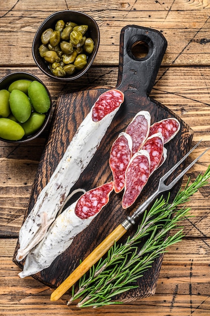 Spanische Tapas Fuet Salami Wurstscheiben mit Oliven und Rosmarin auf einem Holzbrett.