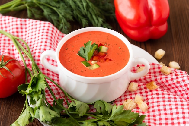 Spanische Tomaten-Gazpacho-Suppe aus frischen Tomaten mit verschiedenen Gewürzen und Kräutern auf hölzernem Hintergrund.