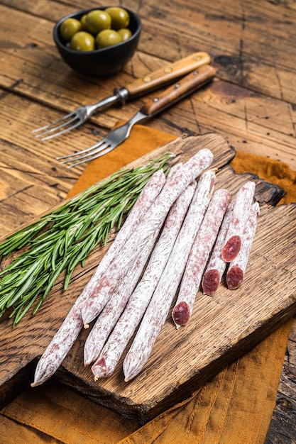 Spanische trockene Salamiwurst Fuet mit Rosmarin auf Holzschneidebrett Holzhintergrund Ansicht von oben